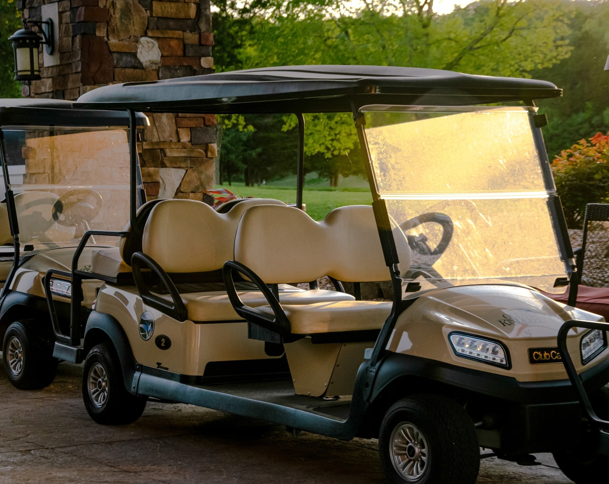 Tan and green golf cart with 4 seats on path with golf course in background. 